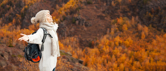 Tourist Woman with Backpack stands with her arms outstretched and enjoys the Autumn mountains - 616972765