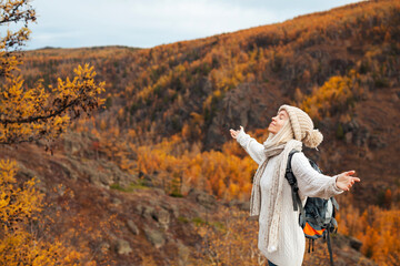 Tourist Woman with Backpack stands with her arms outstretched and enjoys the Autumn mountains