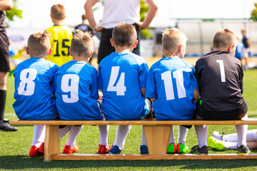 Soccer boys sitting on bench. Football players in youth team sitting on wooden bench during school sports competition tournament. Children sports friendship