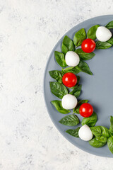 Naklejka na ściany i meble Caprese salad in the form of a Christmas wreath. Festive tomato mozzarella and basil appetizer on grey plate.