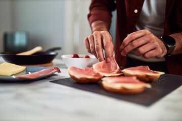 A close-up of a man preparing a sandwich with ham and cheese for breakfast.