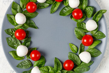 Caprese salad in the form of a Christmas wreath. Festive tomato mozzarella and basil appetizer on grey plate.