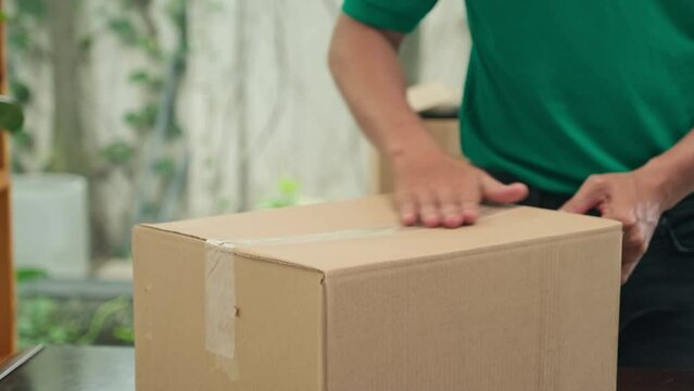 Close up shot of mail worker sealing cardboard box using tape before shipping to client at office