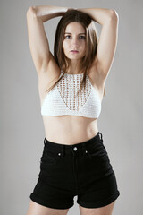 Beautiful pretty young woman poses in a knitted or crocheted white top in photo studio in front of grey background