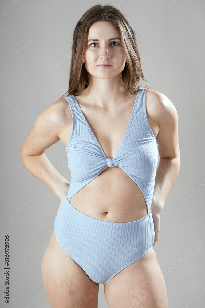 Wall mural young atheltic woman posing in bright blue one-piece swimsuit with open belly in studio in front of 