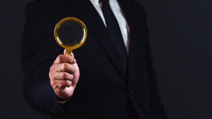 Businessman using magnifying glass against dark background with empty space.