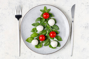 Caprese salad in the form of a Christmas tree. Festive tomato mozzarella and basil appetizer on light plate.