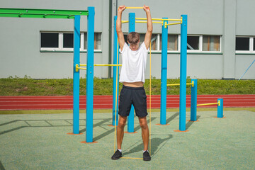 Focused teenager working on his body using resistance rubber performs strength training. Preparing...