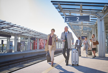Business people walking pulling suitcases on sunny train station platform