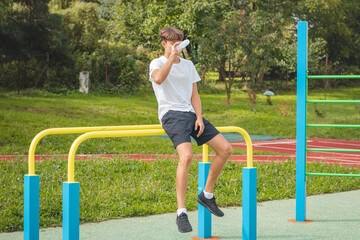 Fototapeta premium Athlete replenishes fluids after a hard workout on the workout field in the intense heat. Training session in an outdoor environment