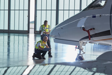 Air traffic control ground crew workers examining corporate jet in airplane hangar