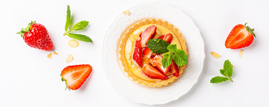 Flat lay banner with strawberry mini cake tartlet with vanilla custard, sprinkled with almond flakes and mint leaves over white background. Concept of homemade healthy sweet pastries. Top view