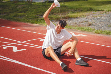 Obraz premium Young athlete refreshes himself with water after a hard workout on the athletic oval in the intense heat. Endurance training. Brown-haired adolescent