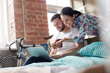 Couple drinking coffee using laptop on bed