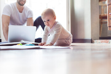 Baby girl playing on floor near father working at laptop