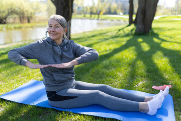 Mature woman in grey sportswear doing yoga in the park