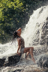 Fototapeta na wymiar Young wet woman sitting on rock near waterfall between water flows.