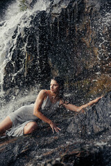 Young wet woman lying on rock near waterfall between water flows.