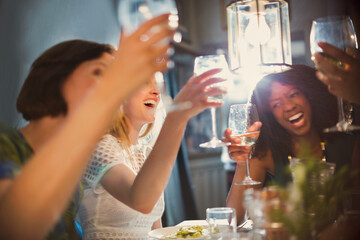 Laughing women friends toasting white wine glasses dining in restaurant