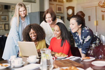 Smiling women friends using laptop at restaurant table