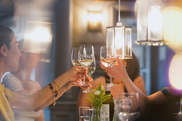 Women friends toasting white wine glasses dining at restaurant table