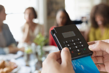 Close up waitress using credit card reader at cafe table
