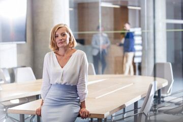 Portrait confident businesswoman leaning on conference room table