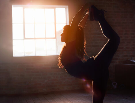 Silhouette female dancer stretching practicing yoga king dancer pose in studio