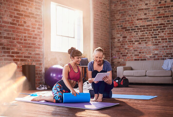 Fitness instructor and young woman using digital tablet in gym studio