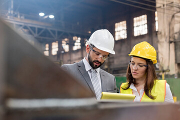 Manager and female steel worker meeting in factory - obrazy, fototapety, plakaty
