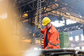 Steel worker fastening chain in factory - obrazy, fototapety, plakaty