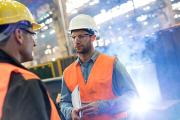 Steel workers talking in factory - Powered by Adobe
