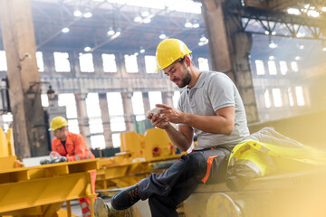 Steel worker texting with cell phone taking a break in factory - obrazy, fototapety, plakaty
