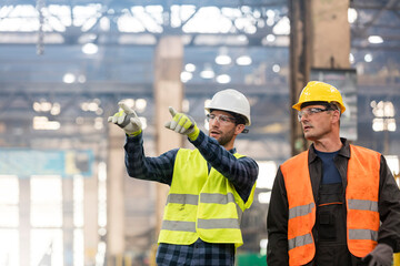 Steel workers talking and pointing in factory - obrazy, fototapety, plakaty