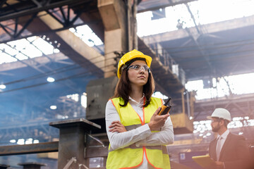 Female steel worker with walkie-talkie in factory - obrazy, fototapety, plakaty