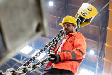 Steel worker holding crane chain in factory - obrazy, fototapety, plakaty