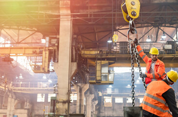 Steel workers operating crane in factory - obrazy, fototapety, plakaty