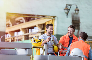 Smiling steel workers enjoying coffee break ins factory - obrazy, fototapety, plakaty