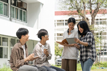 Group of happy students checking results on laptop and tablet while sitting on college campus, concept of education, technology and project work discussion