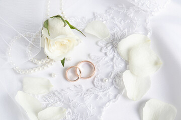 Top view of two gold wedding rings, white rose petals and a flower bud on the bride's wedding veil. invitations, postcards, cover.