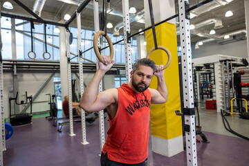 Fit man pulling up on gymnastic rings in gym, training, training his biceps and triceps.