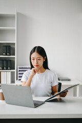 Successful Asian Businesswoman Analyzing Finance on Tablet and Laptop at Office Desk tax, report,...