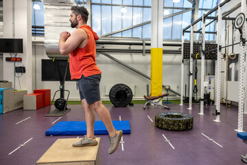 Man in sportswear doing step up workout with wooden box in crossfit gym.