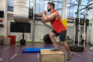 Man in sportswear doing step up workout with wooden box in crossfit gym.