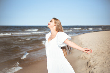 Fototapeta na wymiar Happy smiling beautiful woman is on the ocean beach in a white summer dress, open arms