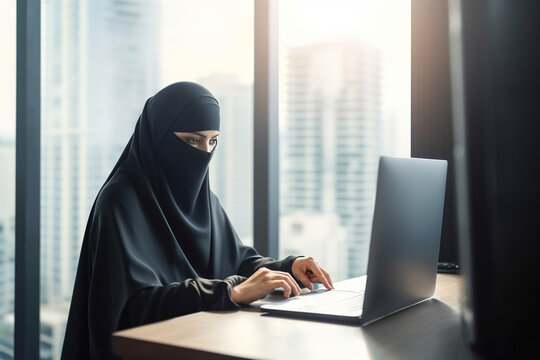 Muslim woman in hijab sitting at a table with a laptop and working in office.
