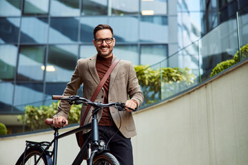 Portrait of a smiling businessman pushing a bicycle in front of the company.