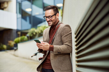 A businessman standing in front of the company and typing messages on the phone.