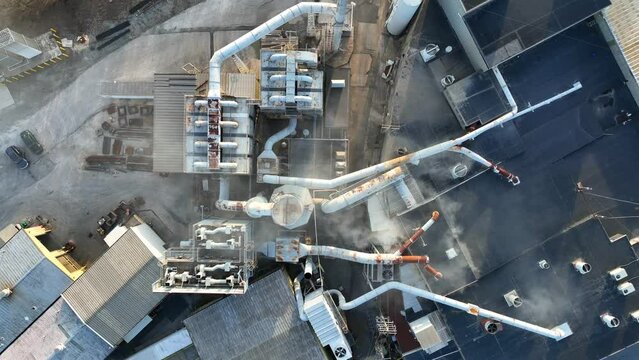 Aerial view of the roof of a metal processing plant.  Industrial cooling and ventilation infrastructure, with steam being released into the setting sky.