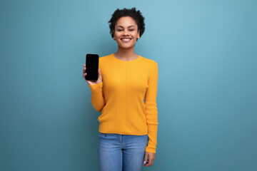 pretty young hispanic woman with black curly hair in a yellow blouse shows the smartphone screen